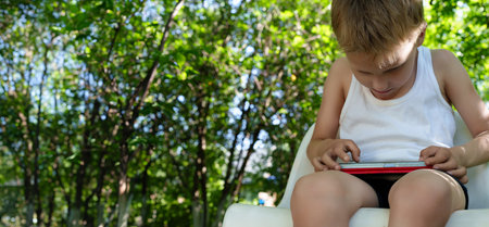 Banner with child captivated by the screen of his smartphone, his posture of a lowered head and slouched shoulders conveying the concerning physical consequences of compulsive mobile device useの写真素材