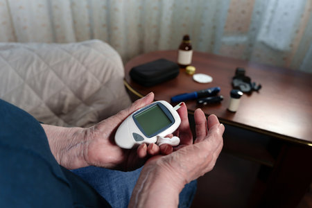 Close-up of an elderly females wrinkled fingers operating a glucometer device to check her blood...