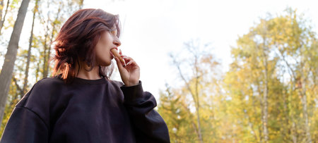 In a cozy autumn park, a teenage girl leisurely eats melting ice cream, her gentle movements create an atmosphere among yellowed leavesの写真素材