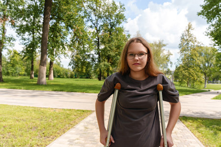 teenage girl stands supported by crutches, her long hair and focused gaze conveying resilience as she navigates mobility challengesの写真素材