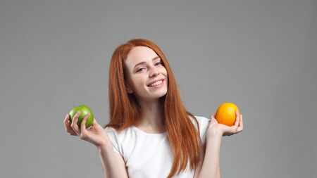 beautiful girl in a white t-shirt smiling holding an Apple in one hand and a grapefruit in the other, on a gray background. Healthy food, delicious fruits.の写真素材