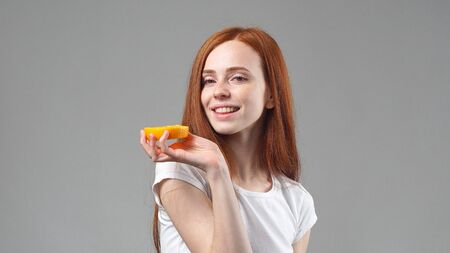 Beautiful young girl holding a glass of orange juice and a piece of orange.の写真素材