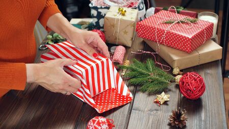 Closeup of woman's hands while wrapping Christmas present, on wood table background.の写真素材