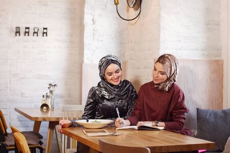 two Muslim business ladies met in a cafe and discuss working moments writing everything in a...