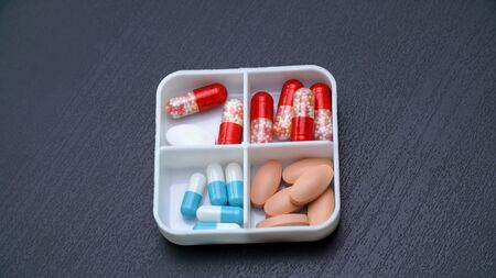 A set of colored tablets in a plastic box for several days, isolated on a dark background.の写真素材