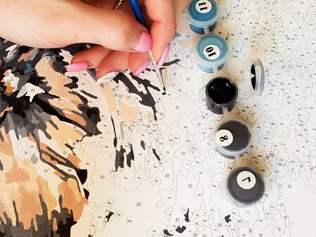 womans hand draws a brush painting by numbers on the canvas.の写真素材