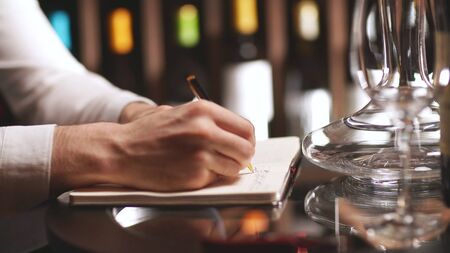 male wine steward makes an inventory of wine in the store, writes some notes in a notebook next to...