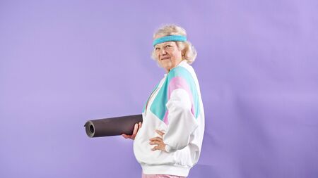 sporty, elegant Mature woman holds a yoga Mat in her hands while posing in a Studio against an isolated background.の写真素材