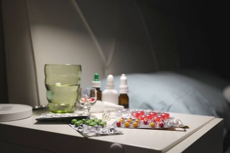 Medicines, medicines, tablets, nose drops, napkins and a glass of water on the bedside table in modern apartments. Concept of home treatment of coronavirus.の写真素材