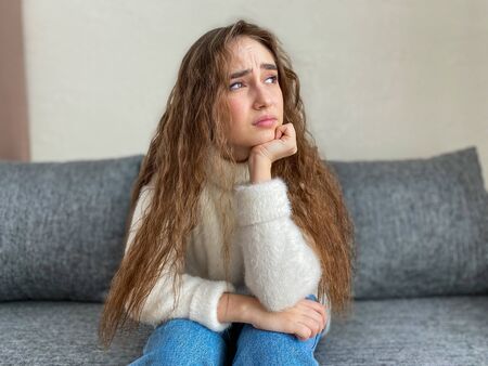 Depression a young woman with long hair is sitting on the sofa in her living room.