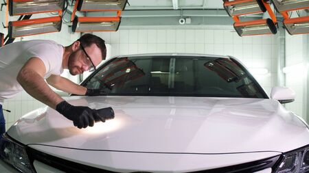 Man in gloves car polishing specialist checks the result of polishing with a flashlight.