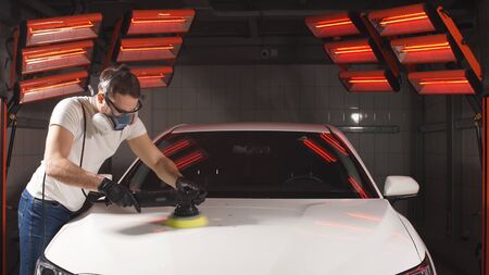man in glasses and a mask, a respirator holds a polisher in his hand and polishes the car with...