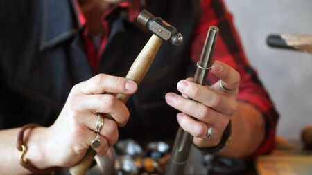 Jeweler in hand holding a hammer for making jewelry. Close up.