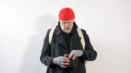 homeless man, a pensioner, an old man with a gray beard in a coat and a red hat on an isolated white background.の写真素材
