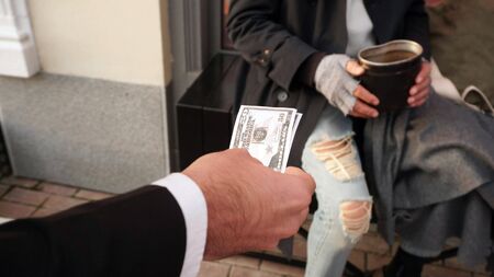 People reach out with money, dollars to a homeless person, a beggar to help, to give money for a...