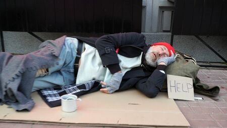 Elderly man, old man, beggar, freezing in the street, drinking hot water to keep warm, sleeping on cardboard in the street.の写真素材