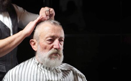 gray-Haired pensioner sits in a Barber shop, barbershop on a haircut. A Barber cuts the hair of an elderly old man, a man aged.の写真素材