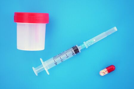 A medical syringe and a plastic container, a test box on an isolated blue, bright background. Delivery of biomaterial.の写真素材