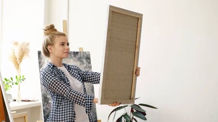 Happy young woman holds a canvas with a finished picture on it.の写真素材