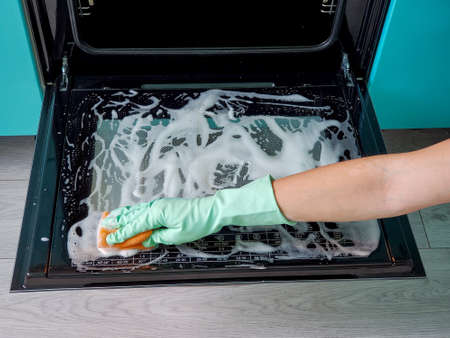 Woman in protective gloves washes the oven door from the inside. House cleaning.の写真素材