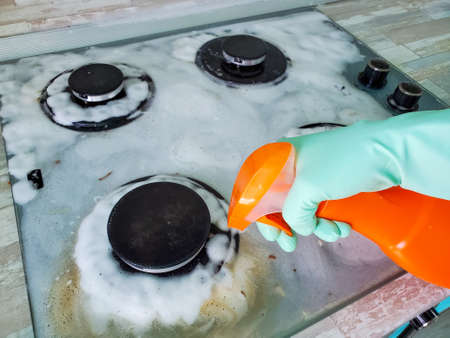 image of a gas stove in foam and womens hands in rubber gloves holding detergent.の写真素材