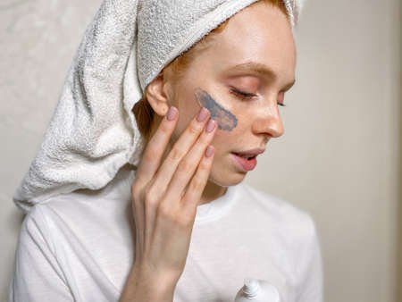 Attractive woman after a shower in a towel on her head does Spa treatments puts a cosmetic mask on her face.の写真素材