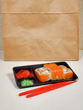 Delicious sushi rolls are served in plastic packaging on an isolated white table background.