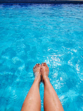 Slender female legs in the bright blue water of the pool on a sunny dayの写真素材