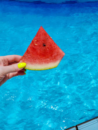 A piece of watermelon on the background of a blue pool on a sunny summer day. the concept of summer and recreationの写真素材