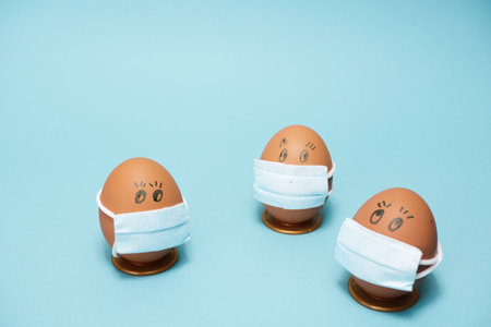 Easter eggs with virus protection concepts. Easter eggs in a medical mask to decorate the Easter holidays. On a blue background with copyspace.の写真素材