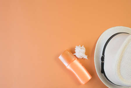 Top view of seashells, sunscreen and hats with copyspace. Summer concept. Orange background. flat...