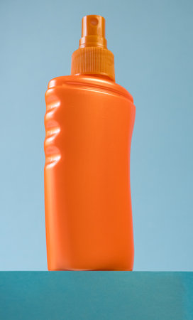 Orange bottle of sunscreen on the podium on a blue background. Summer time on the beach with sun cream. Place for your text. Summer skin protection. Layout.の写真素材