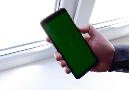 The hands of a young woman with a green-screen phone and a cup of coffee at the table. Chromakey for...