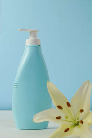 Creative still life makeup photo with blue cosmetic bottle with dispenser and fresh lily flower on...