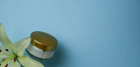 cosmetic jar of cream and yellow lily flower on blue boomの写真素材