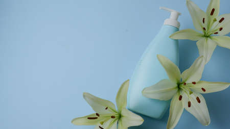 Creative still life makeup photo with blue cosmetic bottle with dispenser and fresh lily lights on blue background. View from above.の写真素材