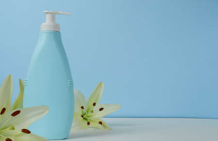 Creative still life makeup photo with blue cosmetic bottle with dispenser and fresh lily flowers on a blue background. With space for text on the right.の写真素材