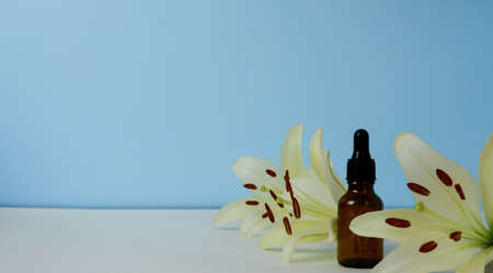 brown glass bottle with cosmetic oil and lily flowers on a blue background.の写真素材