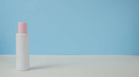 White jar of cream with a pink lid on a blue background, on a white table. With space for text on...