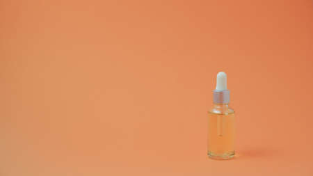 Anti-aging serum in a glass bottle with a dropper on an orange background. Liquid face serum with collagen and peptides. Skin care essence for beautiful and healthy skin.の写真素材