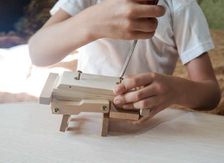 close-up of a boy's hand assembles a wooden toy car with a screwdriver on a wooden table at homeの写真素材