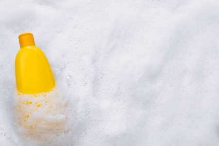 Mockup of a yellow plastic tube with moisturizer, shower gel, shampoo or facial cleanser and gentle soap suds with bubbles on a white background, top view. Medical spa beauty skin care cosmetic productの写真素材