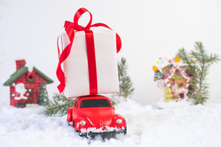 Volgograd, Russia - October 15, 2021: Red retro toy car delivering Christmas or New Year gifts against the background of a snowy road, houses and Christmas trees in the backgroundのeditorial素材