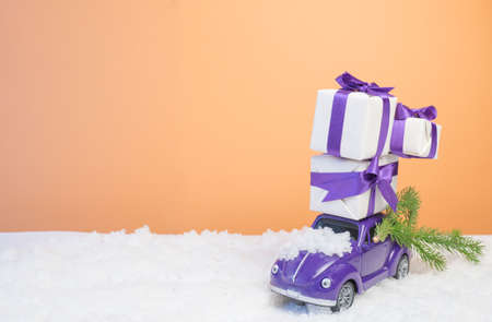 Christmas card concept. Christmas tiny car with gift boxes and a Christmas tree on an orange background with white snowのeditorial素材