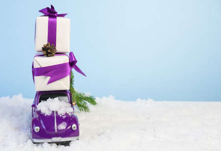 Volgograd, Russia - October 15, 2021: Small purple retro toy car with gift boxes by a Christmas tree on a blue background with white snow. Christmas, birthday, valentine's day, delivery conceptのeditorial素材