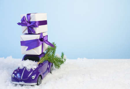 Volgograd, Russia - October 15, 2021: Small purple retro toy car with gift boxes by a Christmas tree on a blue background with white snow. Christmas, birthday, valentine's day, delivery conceptのeditorial素材