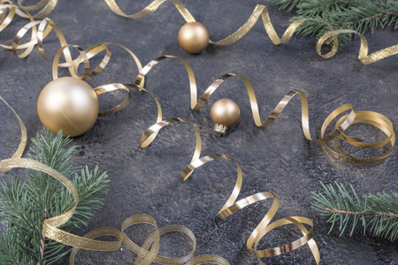 Christmas composition of yellow Christmas balls, fir branches and a gold ribbon on a black with gold embossed background.の写真素材