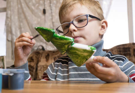 A little boy decorates a hand-made Christmas tree with pine cones and at the same time plays funny