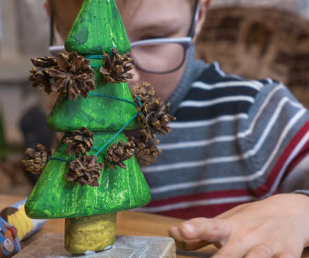 A little boy decorates a hand-made Christmas tree with pine cones and at the same time plays funny.の写真素材