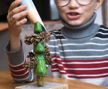 A little boy decorates a hand-made Christmas tree with pine cones and at the same time plays funnyの写真素材